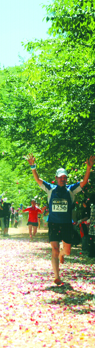 황톳길 맨발마라톤 13㎞ 코스를 내달린 한 참가자가 두 손을 번쩍 들고서 뿌려놓은 꽃잎을 즈려밟으며 결승점에 들어서고 있다.