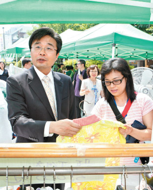 김우영 은평구청장이 지난 6일 사랑나눔 알뜰바자회에서 물건을 사는 주부를 도우며 서민들의 애환을 듣고 있다.