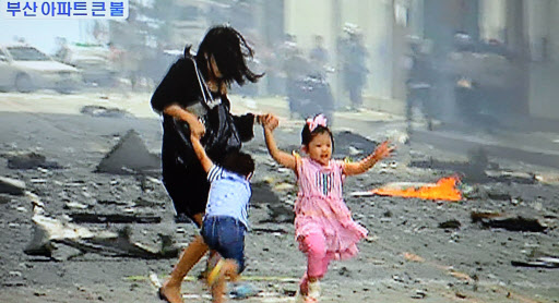 1일 오전 부산시 해운대구 우신골든스위트 화재현장에서 한 여성이 아이들을 데리고 고층건물에서 쏟아져 내린 화재 잔해물들을 피해 대피하고 있다. 부산 연합뉴스