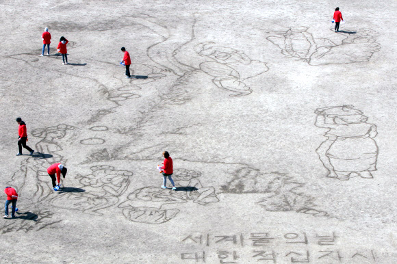 대한적십자사와 서울시립대학교 미술대학생 7명들이 ‘세계 물의 날’을 맞아 21일 서울 송파구 탄천 축구장에서 물로 신윤복의 ‘단오풍정’을 그려내고 있다.  연합뉴스