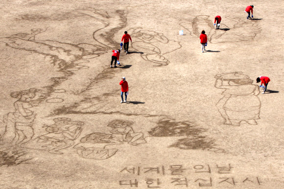 대한적십자사와 서울시립대학교 미술대학생 7명들이 ‘세계 물의 날’을 맞아 21일 서울 송파구 탄천 축구장에서 물로 신윤복의 ‘단오풍정’을 그려내고 있다.  연합뉴스