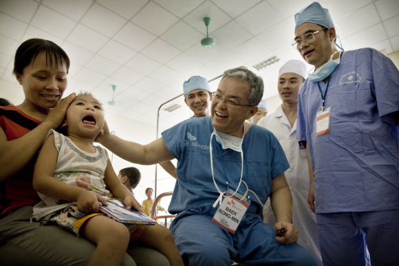 베트남 탄호아 지역 병원에서 수술할 당시 백롱민(가운데) 교수가 수술 후 회진 중에 한 어린이를 쓰다듬으며 웃고 있다.  분당서울대병원 제공