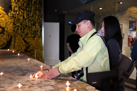 노무현 전 대통령 3주기를 맞아 김해 봉하마을 추모관을 찾은 추모객들이 노란 리본으로 만든 고인의 사진 앞에 촛불을 밝히고 있다. 연합뉴스