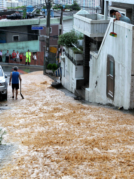 부산 지역에 188mm비가 내린 15일 오후 부산 진구 전포동 진남로에 인근 야산에서 쏟아진 토사가 흘러내려 저지대 주민들이 집안으로 들어온 흙탕물을 치우고 있다. 연합뉴스