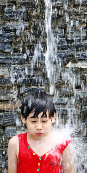 무더위가 기승을 부린 24일 서울시 송파구 오금동에서 어린이가 벽에서 흐르는 폭포로 더위를 식히고 있다.  연합뉴스