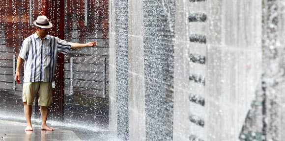 무더위가 기승을 부린 24일 서울시 송파구 오금동에서 중절모를 쓴 할아버지가 벽에서 흐르는 폭포로 더위를 식히고 있다. 연합뉴스