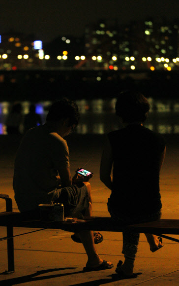 런던올림픽 한국대표팀의 금빛사냥 첫 날인 29일 새벽, 열대야를 피해 한강 시민공원에 나온 시민들이 스마트폰으로 남자사격 진종오의 금메달 소식을 보고 있다. 이날 4개의 금메달을 노렸던 한국은 진종오의 금메달과 박태환의 400m 은메달에 만족해야 했다. 연합뉴스