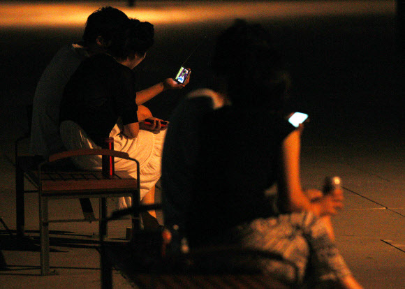 런던올림픽 한국대표팀의 금빛사냥 첫 날인 29일 새벽, 열대야를 피해 한강 시민공원에 나온 시민들이 스마트폰으로 남자사격 진종오의 금메달 소식을 보고 있다. 이날 4개의 금메달을 노렸던 한국은 진종오의 금메달과 박태환의 400m 은메달에 만족해야 했다. 연합뉴스