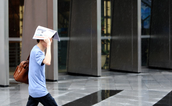 30일 오후 서울 중구 삼성생명 앞 도보에서 한 시민이 갑작스레 쏟아진 비에 신문으로 머리를 가리고 걸어가고 있다.  연합뉴스