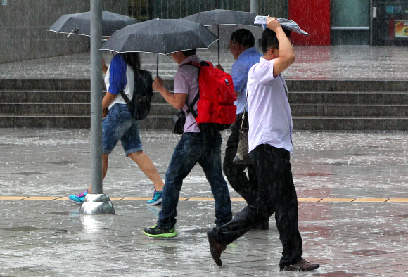 무더위를 식혀주는 ‘깜짝’ 소나기가 내리던 30일 오전 서울시 중구 봉래동 서울역 광장에서 한 시민이 신문지로 비를 피하며 걷고 있다.  연합뉴스
