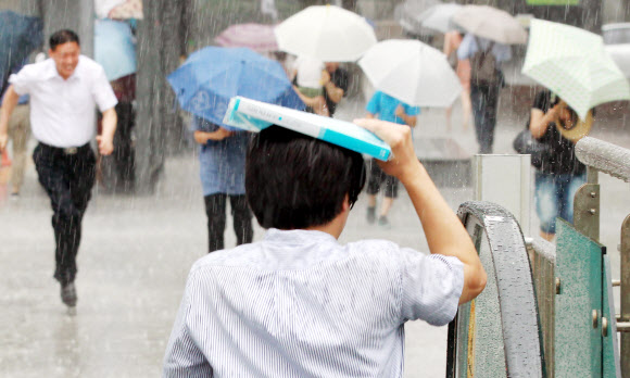 갑자기 많은 양의 소나기가 내린 30일 오전 서울 광화문에 한 시민이 우산 대신 서류보관용 파일로 비를 막아보고 있다.  연합뉴스