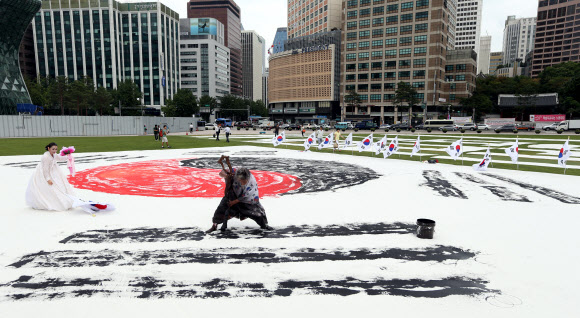 광복절을 하루 앞둔 14일 오후 서울광장에서 한국 서예 퍼포먼스 김동욱 고문이 대형 태극기 그리기 퍼포먼스를 하고 있다. 연합뉴스