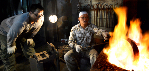 전통 방짜 유기 이수자 이광운(왼쪽)씨가 전수 조교인 이춘복씨에게 불에 달구고 망치로 두드려서 그릇의 형태를 만드는 전통 기법을 배우고 있다.