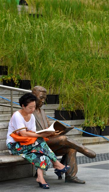 독서는 이제 언제 어디서나 즐길 수 있는 문화활동이 됐다. 한 중년 여성이 서울 세종로 세종문화회관 앞의 책 읽는 사람 동상 옆에서 독서를 하고 있다.  서울신문 포토라이브러리