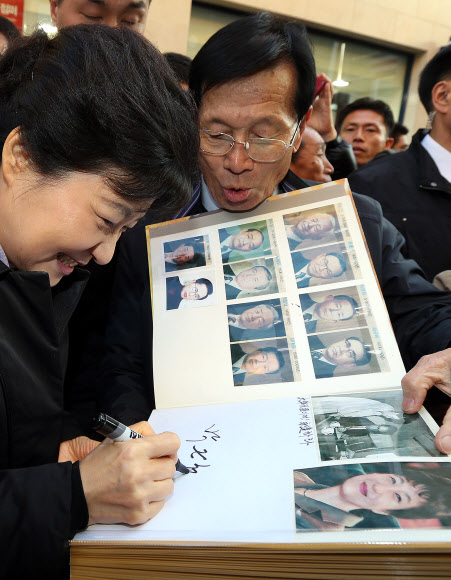 새누리당 박근혜 대선후보가 14일 오후 충북 충주시 성서동 차없는 거리를 방문, 한 지지자의 역대 대통령과 박 후보의 사진을 모은 사진첩에 사인을 해주고 있다 연합뉴스