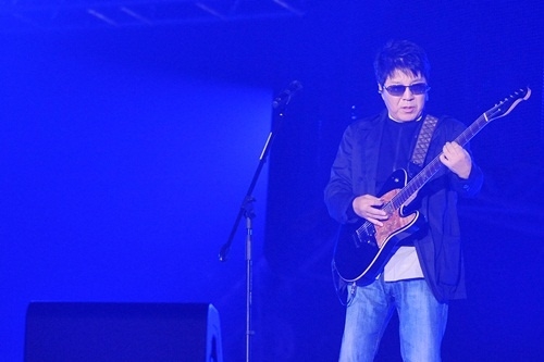 가수 조용필이 무대 위에서 기타를 연주하고 있다.