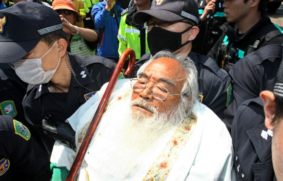 25일 오전 제주해군기지(민군복합형 관광미항) 공사장 앞에서 ‘제주군사기지 저지와 평화의 섬 실현을 위한 범도민대책위원회’의 기자회견이 열린 가운데 해군기지 공사장 앞을 가로막아선 문정현 신부가 경찰에 의해 도로 밖으로 끌려나오고 있다.  연합뉴스