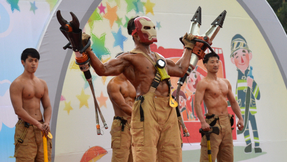 2일 서울 여의도공원 문화광장에서 열린 서울시 최강 몸짱 소방관 선발대회에 참가한 한 소방관이 아이언맨 마스크를 쓰고 동력절단기를 든 채 근육을 뽐내고 있다.  