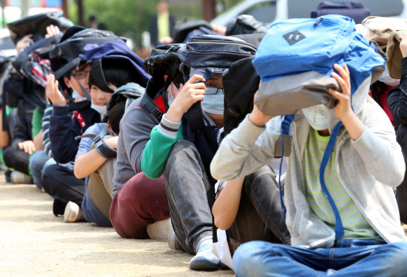 전국적으로 지진대비 민방공훈련이 열린 7일 오후 서울 용산구 효창동 금양초등학교에서 훈련 사이렌이 울리자 학생들이 가방을 머리에 뒤집어 쓴 채 운동장에 앉아있다. 연합뉴스