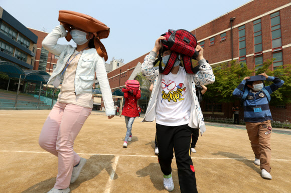 전국적으로 지진대비 민방공훈련이 열린 7일 오후 서울 용산구 효창동 금양초등학교에서 훈련 사이렌이 울리자 학생들이 가방을 머리에 뒤집어 쓴 채 건물 밖으로 뛰어나오고 있다.  연합뉴스