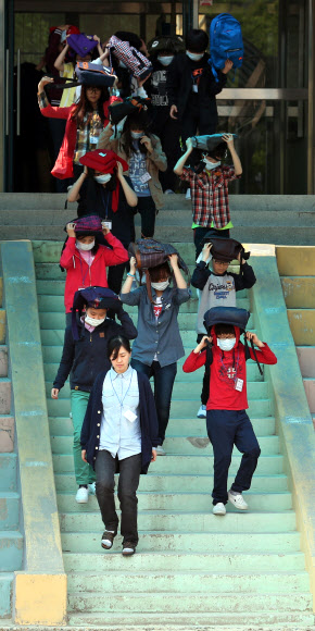 전국적으로 지진대비 민방공훈련이 열린 7일 오후 서울 용산구 효창동 금양초등학교에서 훈련 사이렌이 울리자 학생들이 가방을 머리에 뒤집어 쓴 채 건물 밖으로 뛰어나오고 있다. 연합뉴스