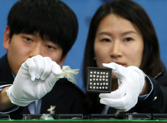 관세청 인천공항세관은 인천공항을 통해 7억 원 상당의 다이아몬드를 밀수하려 한 혐의(관세법 위반)로 홍콩인 L(50·여)씨를 구속했다고 10일 밝혔다. L씨는 지난 4일 1캐럿 이상 다이아몬드 3개를 포함해 총 1천32개, 342캐럿 상당의 다이아몬드를 콘돔으로 포장해 항문 속에 숨겨 밀반입하려 한 혐의를 받고 있다.사진은 10일 인천공항세관 수출입통관청사에서 인천공항세관 관계자들이 압수한 다이아몬드와 다이아몬드를 포장했던 콘돔을 살펴보는 모습.    연합뉴스