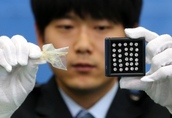 관세청 인천공항세관은 인천공항을 통해 7억 원 상당의 다이아몬드를 밀수하려 한 혐의(관세법 위반)로 홍콩인 L(50·여)씨를 구속했다고 10일 밝혔다. L씨는 지난 4일 1캐럿 이상 다이아몬드 3개를 포함해 총 1천32개, 342캐럿 상당의 다이아몬드를 콘돔으로 포장해 항문 속에 숨겨 밀반입하려 한 혐의를 받고 있다.사진은 10일 인천공항세관 수출입통관청사에서 인천공항세관 관계자가 압수한 다이아몬드와 다이아몬드를 포장했던 콘돔을 살펴보는 모습.   연합뉴스