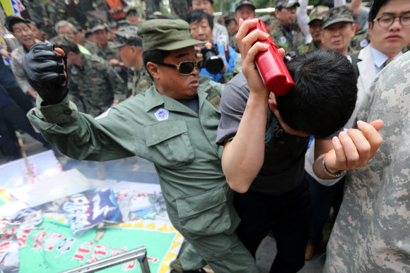 주한일본대사관 앞에서 한 대한민국고엽제전우회 회원이 아베 일본 총리와 하시모토 오사카 시장의 얼굴이 인쇄된 현수막 화형식을 막으려 소화기를 뿌린 경찰을 주먹으로 때리고 있다. 연합뉴스