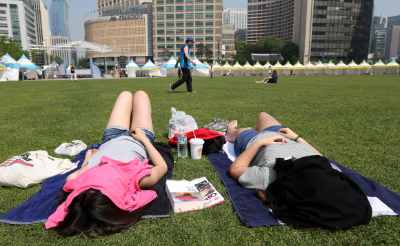 서울의 기온이 30도까지 올라간 23일 오후 서울광장에서 시민이 일광욕을 즐기고 있다.  연합뉴스
