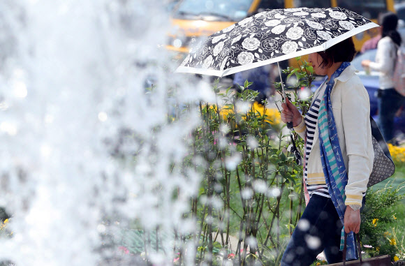 서울의 기온이 30도까지 올라간 23일 오후 서울광장에서 양산을 쓴 한 시민이 분수 뒤를 지나고 있다. 연합뉴스