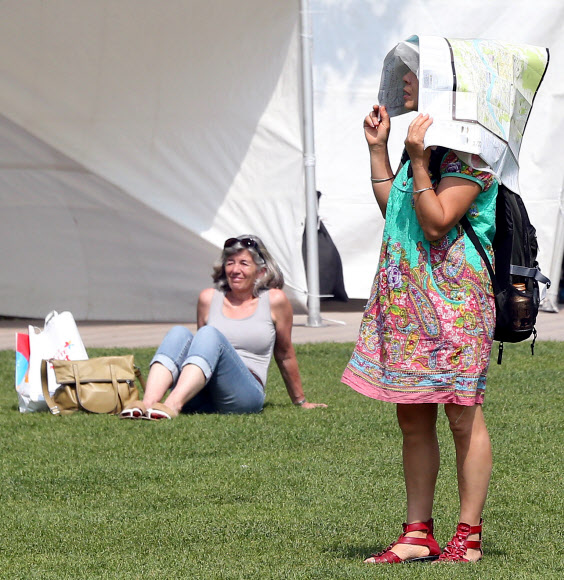 서울의 기온이 30도까지 올라간 23일 오후 서울광장에서 일광욕을 즐기는 외국인 앞으로 한 시민이 종이로 햇빛을 가리며 지나가고 있다.  연합뉴스