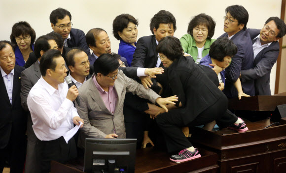 김오영 경남도의회 의장이 11일 오후 도의회 본회의장에서 마이크를 잡고 동료 새누리당 의원과 의회 사무처 직원의 보호 속에 진주의료원 해산 조례를 날치기 통과하고 있다.민주개혁연대 소속 도의원들이 날치기를 저지하기 위해 온몸으로 저항했지만 숫적으로 훨씬 많은 새누리당 의원들에 의해 저지됐다. 연합뉴스