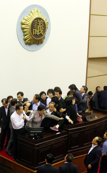 진주의료원 해산 조례 날치기 통과 김오영 경남도의회 의장이 11일 오후 도의회 본회의장에서 마이크를 잡고 동료 새누리당 의원과 의회 사무처 직원의 보호 속에 진주의료원 해산 조례를 날치기 통과하고 있다.민주개혁연대 소속 도의원들이 날치기를 저지하기 위해 온몸으로 저항했지만 숫적으로 훨씬 많은 새누리당 의원들에 의해 저지됐다. 연합뉴스