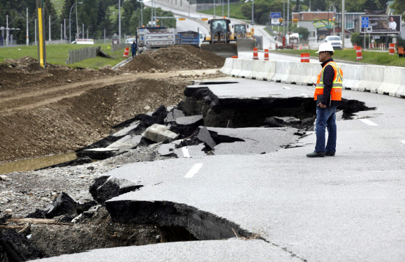 지난 24일 캐나다 앨버타주 캘거리에서 한 인부가 폭우로 유실된 도로를 바라보고 있다.  캘거리 AP 연합뉴스   