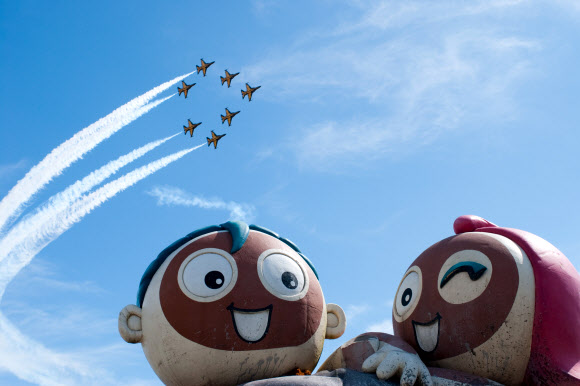 ‘제16회 보령머드축제’ 개막식이 열린 19일 충남 보령시 신흑동 대천해수욕장 상공에서 공군 특수비행팀 ‘블랙이글스’가 펼치는 에어쇼를  온몸에 머드를 바른 관광객들이 감상하고 있다.  연합뉴스