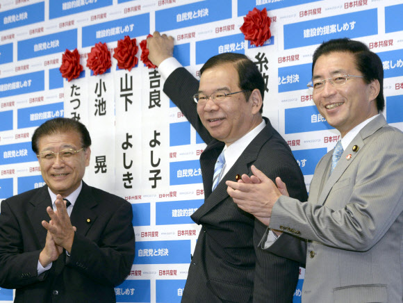 일본공산당의 시이 가즈오(志位和夫·가운데) 위원장이 21일 도쿄 센다가야(千馱ケ谷)의 당 본부에서 당선자 이름 옆에 꽃을 달며 웃고 있다. 연합뉴스