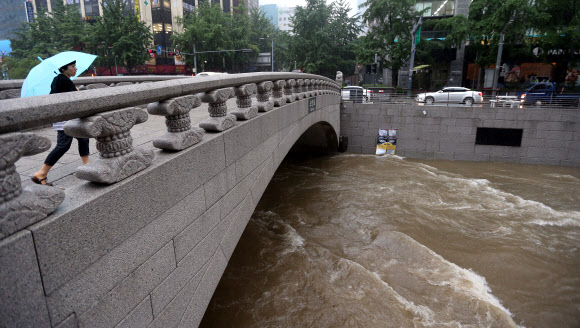 주말동안 잠시 소강상태를 보였던 장맛비가 다시 시작된 22일 오전 서울 청계천을 지나는 한 시민이 폭우로 불어난 물을 바라보고 있다. 연합뉴스