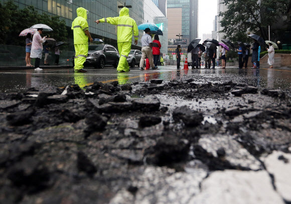 새벽부터 집중호우가 내린 22일 오전 서울 서초구 강남역 8번 출구 인근 도로에 ‘포트홀’이 생겨 운전자들의 안전운행을 위협하고 있다.  연합뉴스
