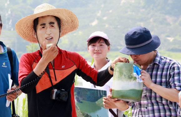 이명박 전 대통령 마스크를 쓴 시민단체 회원이 이미경 국회의원에게 지난주 대구취수장에서 채취한 녹조때문에 짙은 녹색을 띠고 있는 낙동강물을 와인잔에 따라주는 퍼포먼스를 진행하고  있다.  연합뉴스