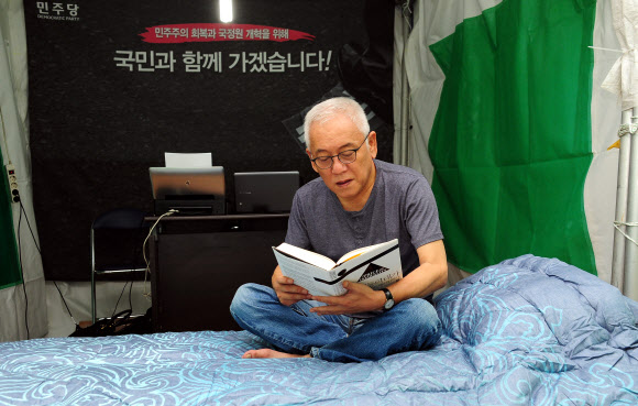 서울광장 ‘노숙투쟁 ‘에 들어간 김한길 민주당 대표가 27일 저녁 서울 중구 태평로 서울시청 앞 광장 국민운동본부 천막 옆에 마련한 별도 천막에서 침대 위에 앉아 책을 읽고 있다.  << 민주당 제공 >>