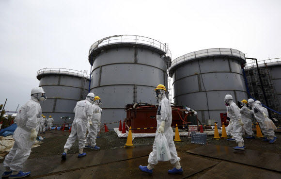 방호복과 방사능 차단 마스크를 착용한 일본 도쿄전력 직원들이 7일 후쿠시마현 오쿠마에 있는 후쿠시마 제1원자력발전소에서 방사능 오염수가 저장돼 있는 탱크 주변을 지나고 있다. 오쿠마 AP 연합뉴스