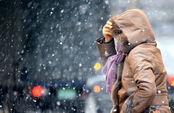 ‘펄펄 눈이 옵니다’ 함박눈이 내린 12일 오전 한 시민이 모자를 쓰고 서울 광화문 거리를 지나고 있다.  연합뉴스