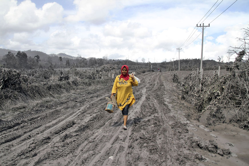 11일(현지시간) 인도네시아 수마트라 북부 시나붕 화산의 활동이 일어나 화산재와 진흙에 덮인 길을 한 여성이 걷고 있다. AP/뉴시스