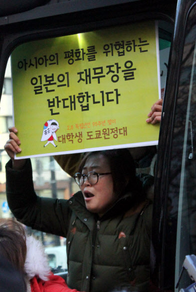 강제로 버스에 태워진 원정대의 한 여성이 일본의 재무장에 반대한다는 피켓을 들고 있다.  연합뉴스