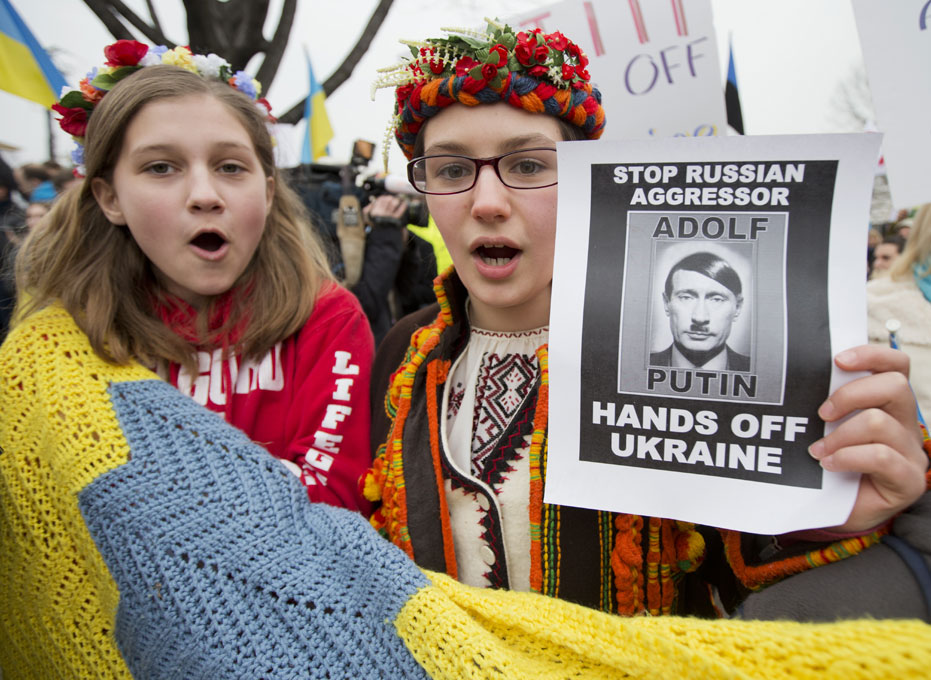 2일(현지시간) 워싱턴 러시아 대사관 앞에서 우크라이나 여성 2명이 러시아의 크림반도 출병에 항의시위를 벌였다. 이들은 블라미르 푸틴 러시아 대통령의 모습을 아돌프 히틀러 처럼 변조하고 “아돌프 푸틴은 우크라이나에서 손 떼라”고 쓴 포스터를 보여주고 있다.  워싱턴 =AP/뉴시스