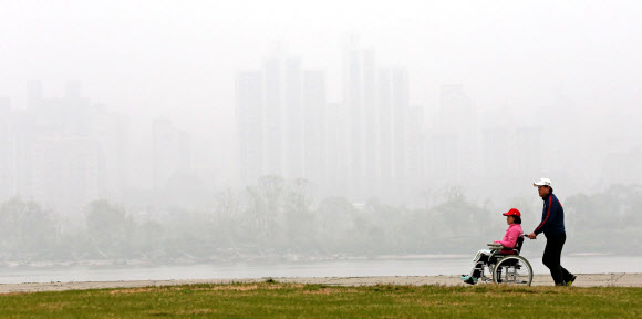 서울지역에 올해 첫 미세먼지 주의보가 발령된 16일 오전 서울 한강을 찾은 한 남성이 부인의 휠체어를 밀며 함께 산책을 하고 있다. 연합뉴스