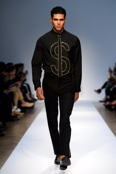 영국 런던에서 16일(현지시간) ‘런던 콜렉션: 맨(London Collections: Men)’ 패션쇼가 열렸다. 이번 패션쇼에서는 2015 봄/여름 컬렉션을 주제로 여러 유명 디자이너들의 의상을 선보였다.  모델이 브랜드 모스키노의 ‘$’가 메인 디자인인 검은 옷을 입고 워킹하고 있다. 사진 ⓒ AFPBBNews=News1/ 온라인뉴스부 iseoul@seoul.co.kr