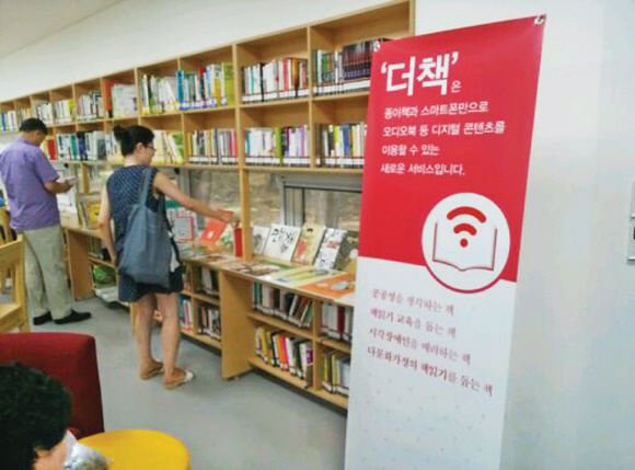 지난달 서울 노원구 상계숲속작은도서관을 찾은 시민들이 더책 서비스가 제공되는 책들을 살펴보고 있다. 근거리무선통신(NFC) 태그를 부착한 종이책에 스마트폰을 대면 오디오북, 동영상 등 디지털 콘텐츠를 함께 즐길 수 있다.  미디어창비 제공