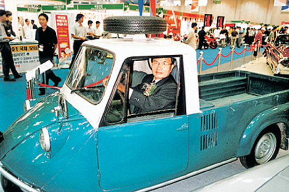 한국 최초의 용달차 사업을 창업한 강병중 넥센타이어 회장이 2001년 국제모터쇼에 전시된 삼륜차를 타고 있다. <자료:강병중 회장 홈페이지, 저서 ‘부산경제를 위한 강병중 회장의 집념’ 중>