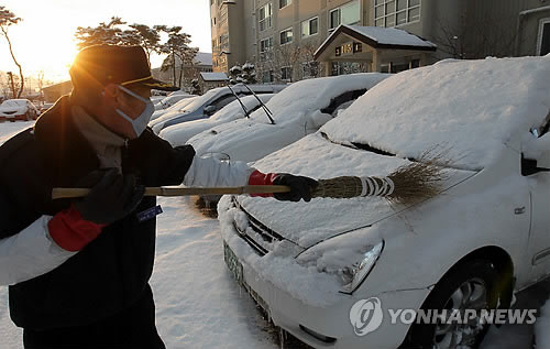 한 아파트에서 경비원이 차 위에 쌓인 눈을 치우고 있다. (연합뉴스 자료사진)